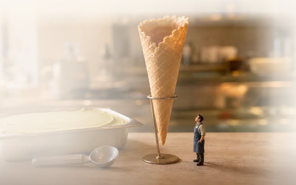 Scoopwright website hero — a miniature artisan beside an empty waffle cone on a gelato counter